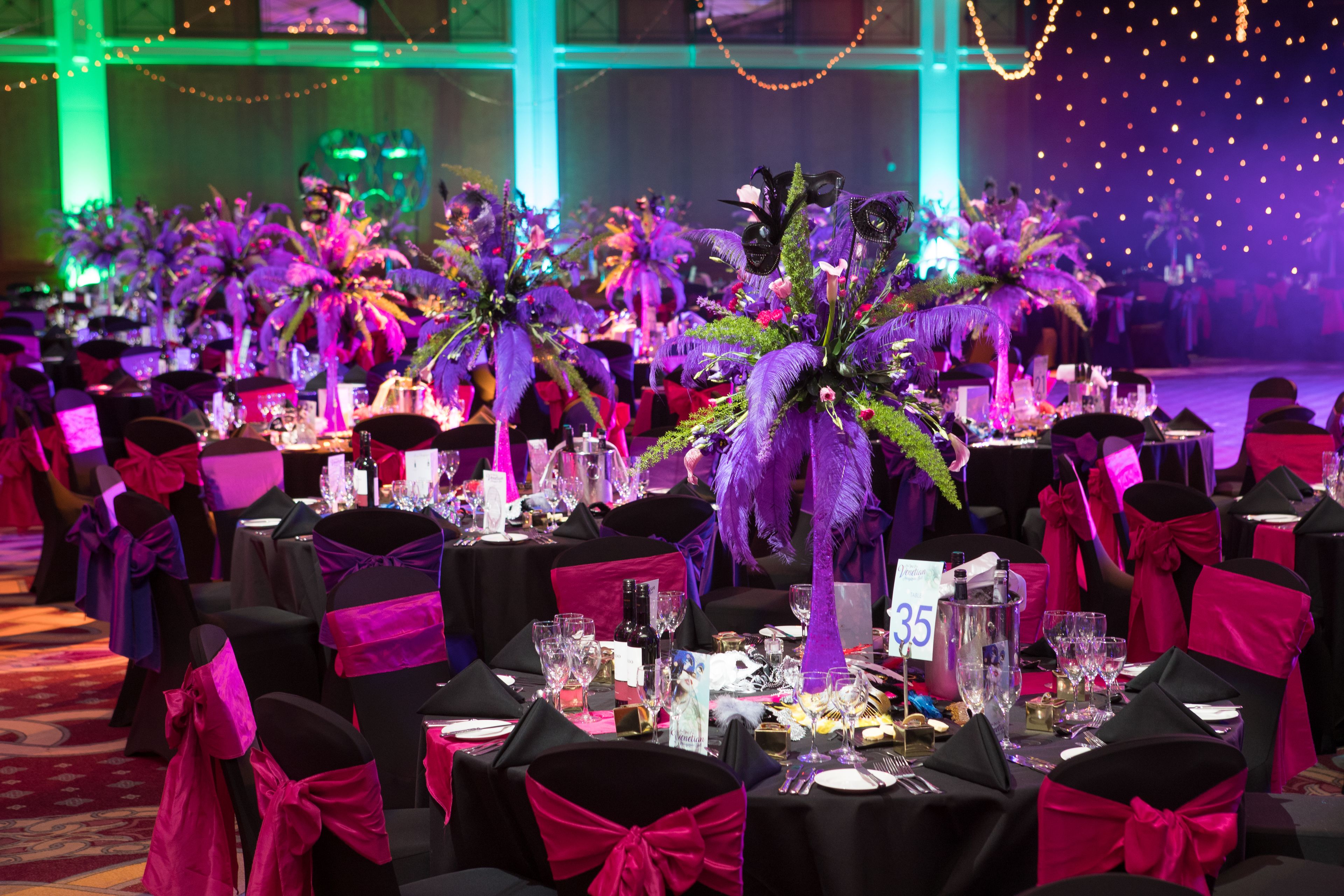 Une salle de banquet où les tables sont dressées pour un événement officiel, décorées de compositions florales et de rubans rouges.
