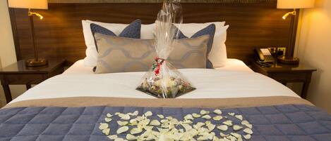 A neatly made bed with a blue quilt, white pillows, and a decorative arrangement of white flowers and a gift bag.