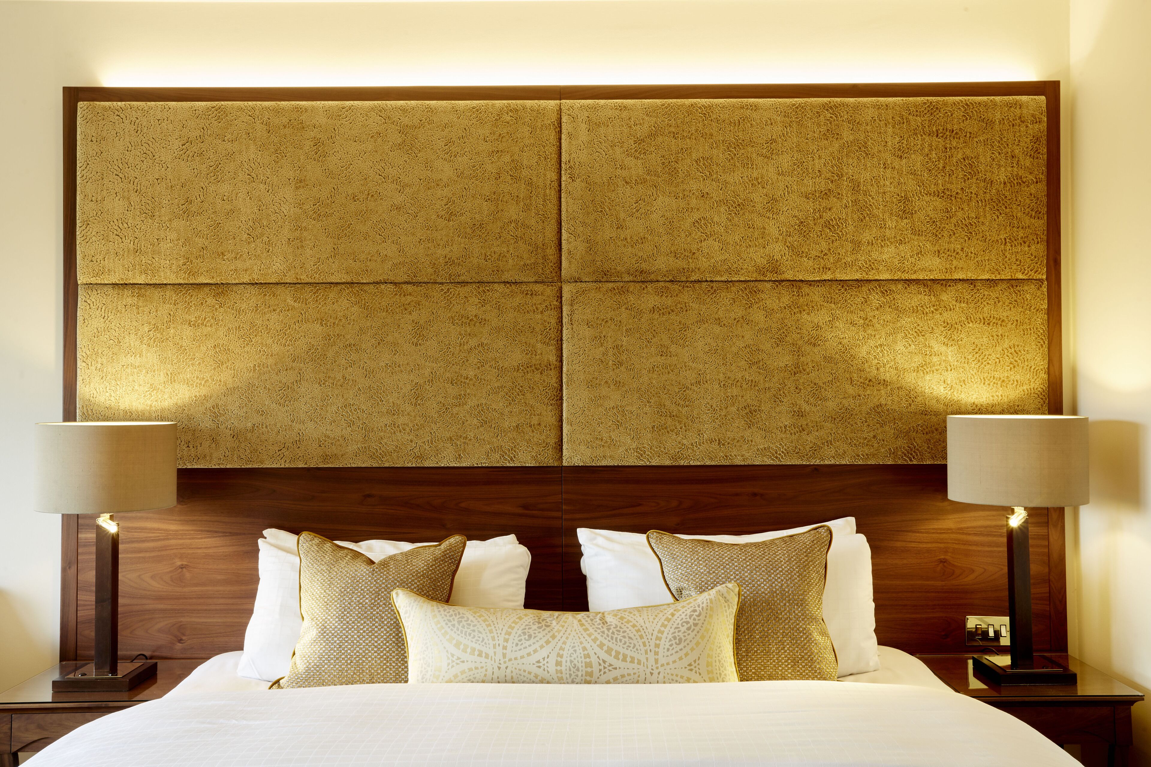 A hotel room with a large bed, two bedside tables with lamps, and a headboard with a textured panel design.