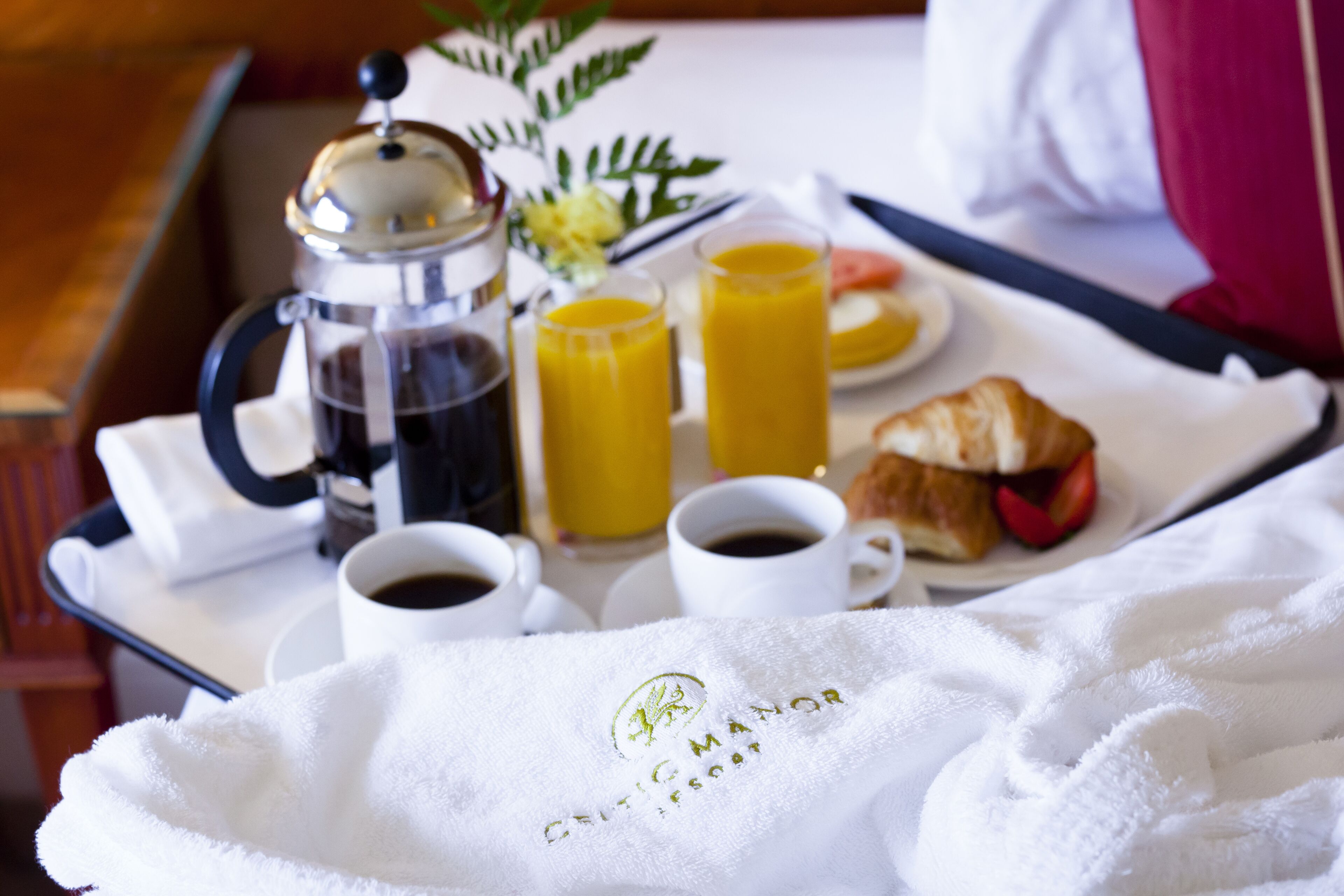 Ett frukostbricka med kaffe, juice, croissant och en handduk med hotellets logotyp.