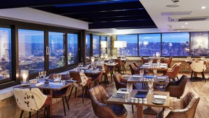 A restaurant with multiple tables and chairs, large windows offering a city view, and a modern interior design. - Celtic Manor Resort (Newport)