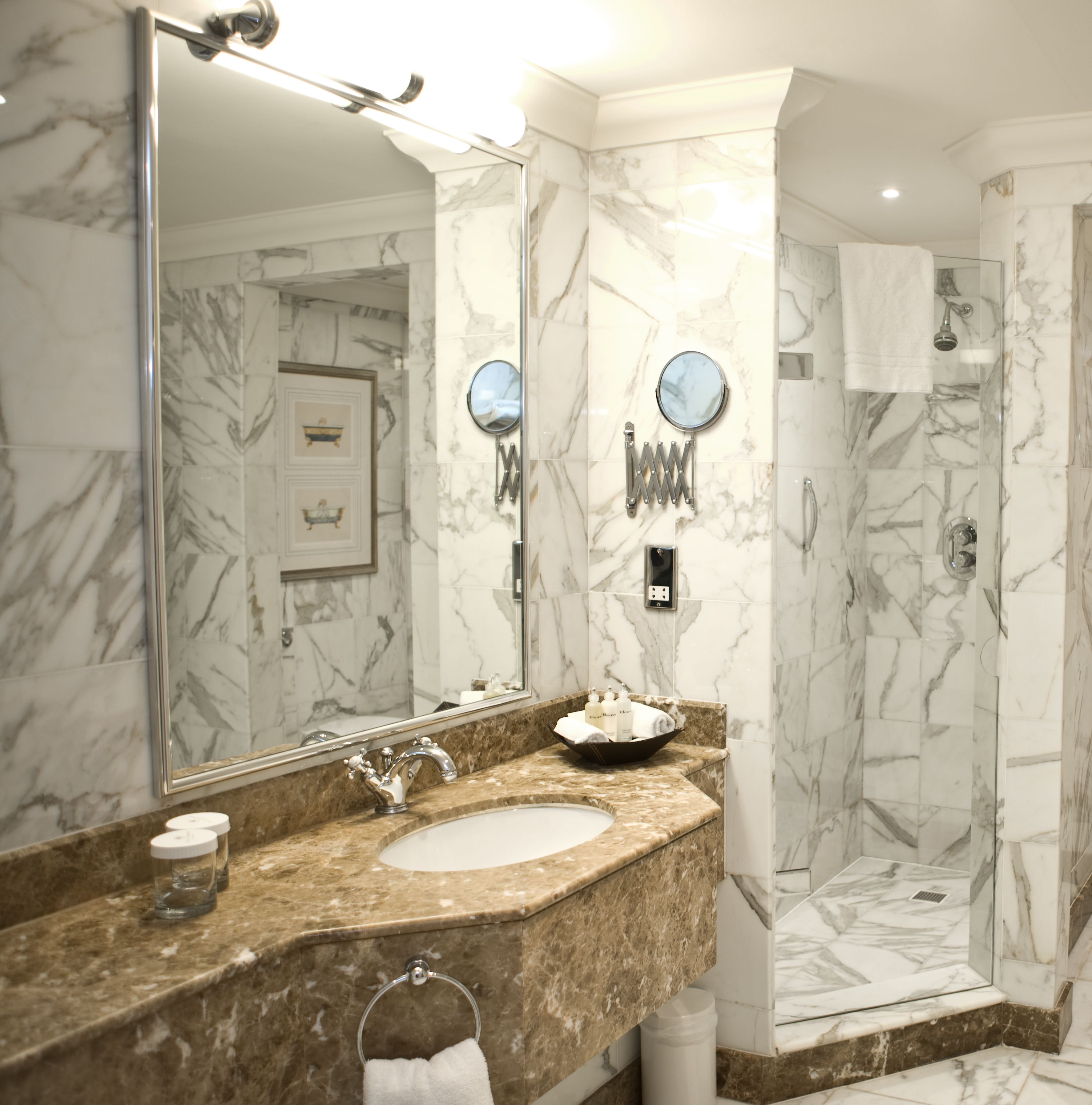 A bathroom with a marble sink, a large mirror, and a walk-in shower.