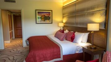 A hotel room with a large bed, two bedside tables with lamps, a headboard, a painting on the wall, and a carpeted floor.