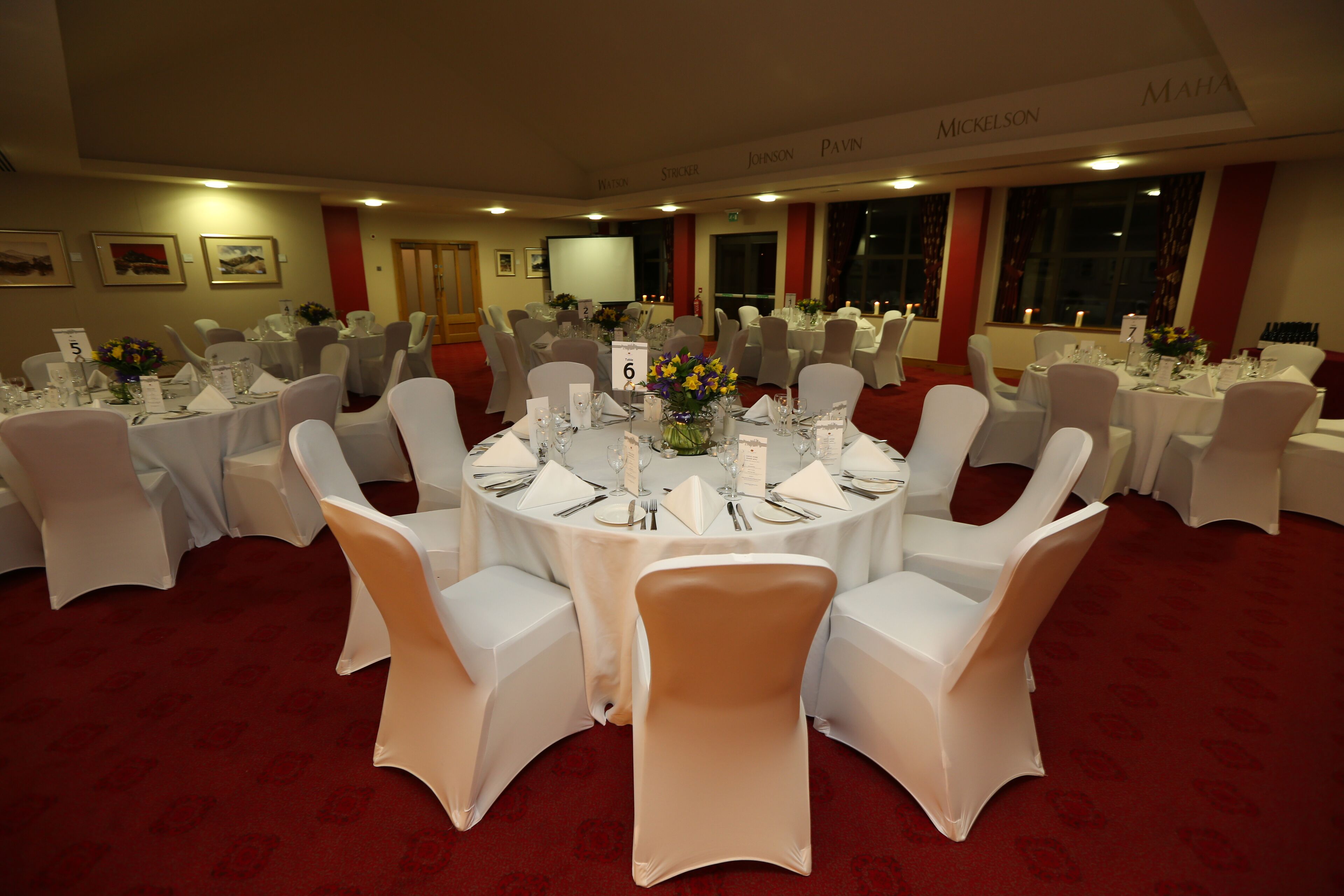 A conference room with round tables, white chairs, and red carpet flooring.