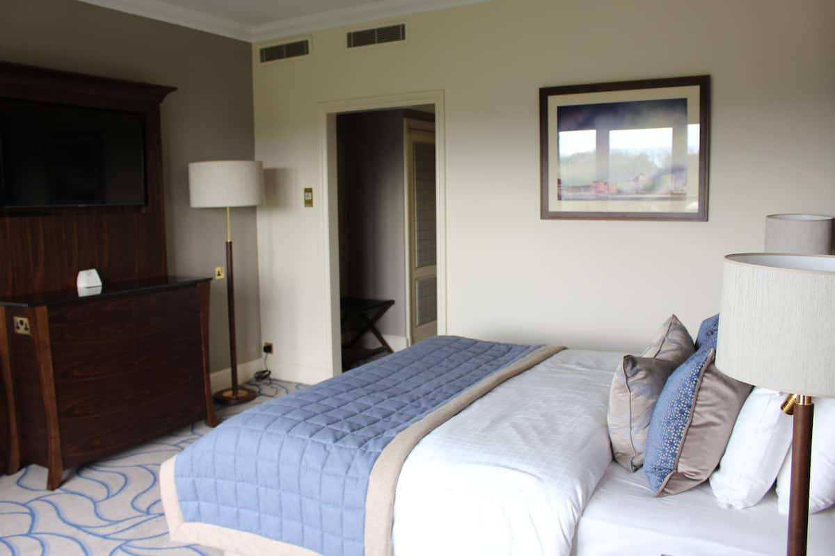 A hotel room with a bed, a dresser, a TV, a lamp, and a painting on the wall.