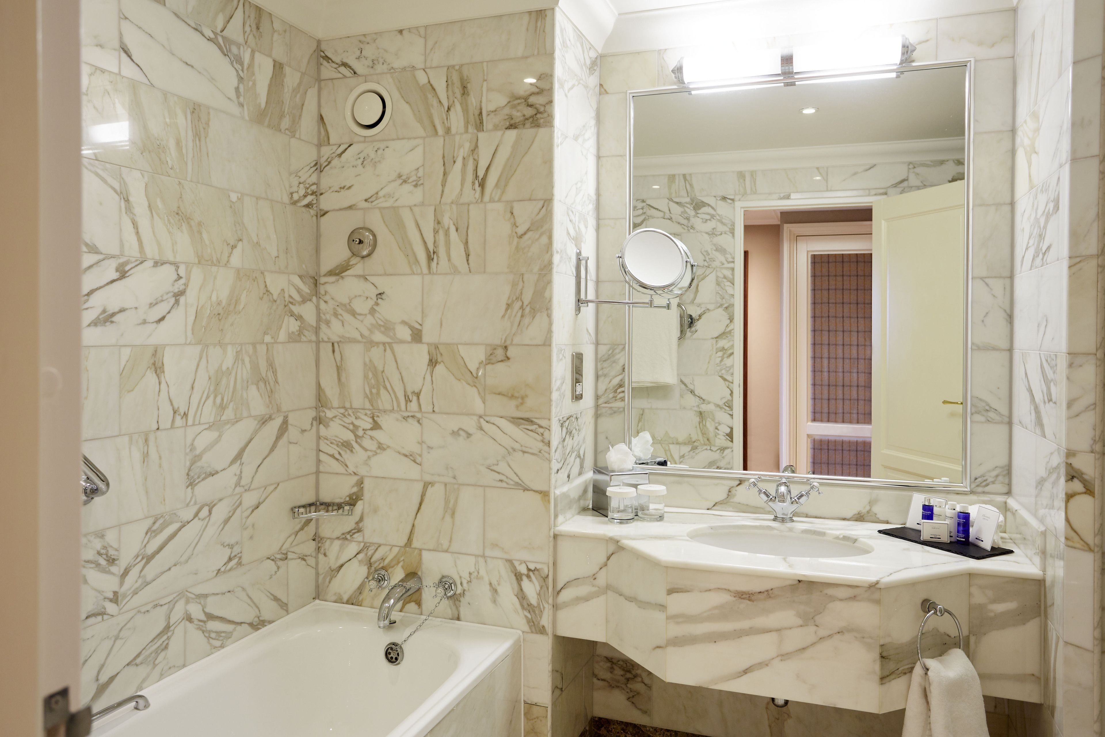 A bathroom with a marble-tiled wall, a bathtub, a sink with a mirror, and a towel rack.