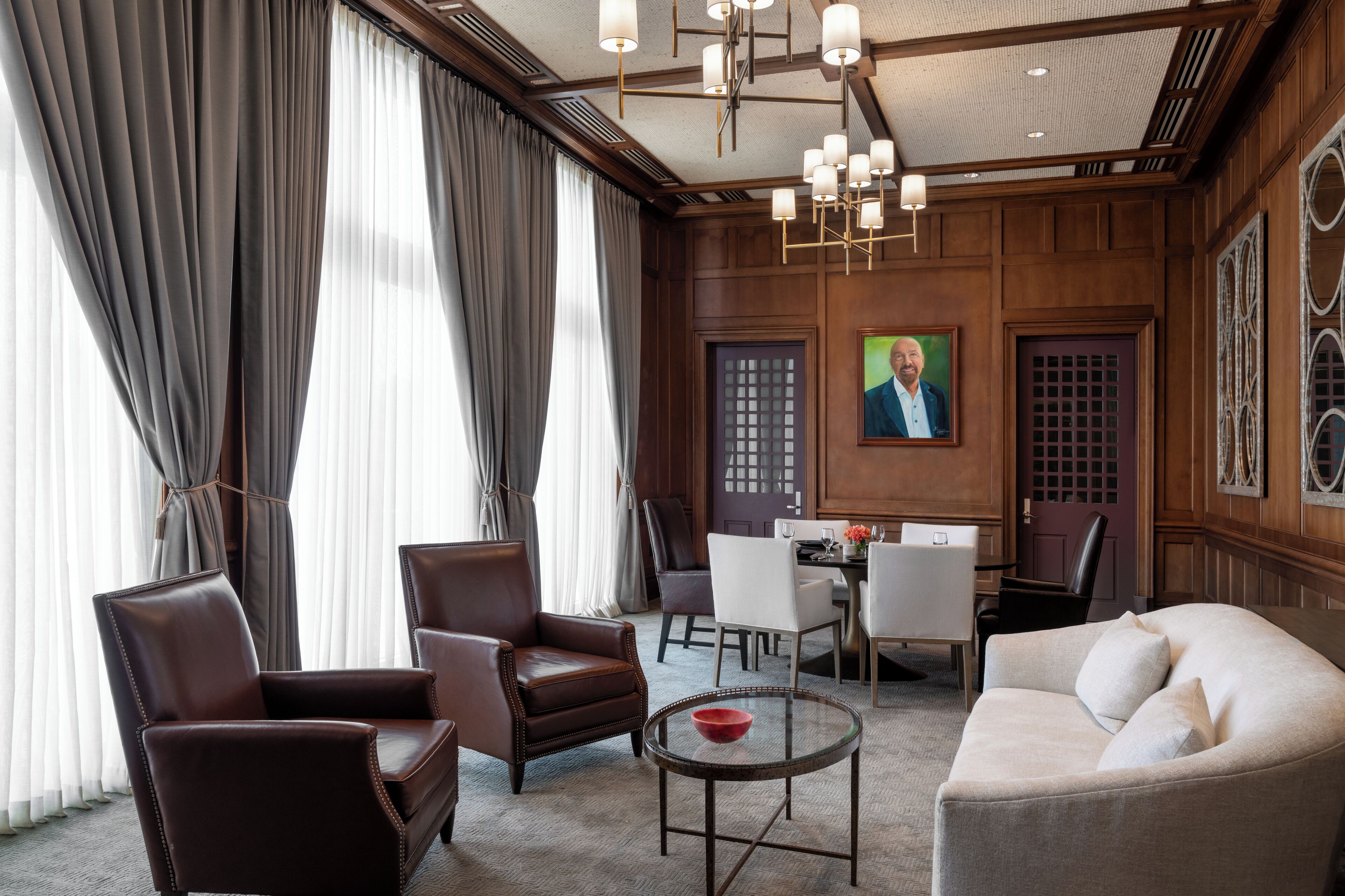 A well-appointed hotel room with leather armchairs, a sofa, a dining area, and a large window with curtains.