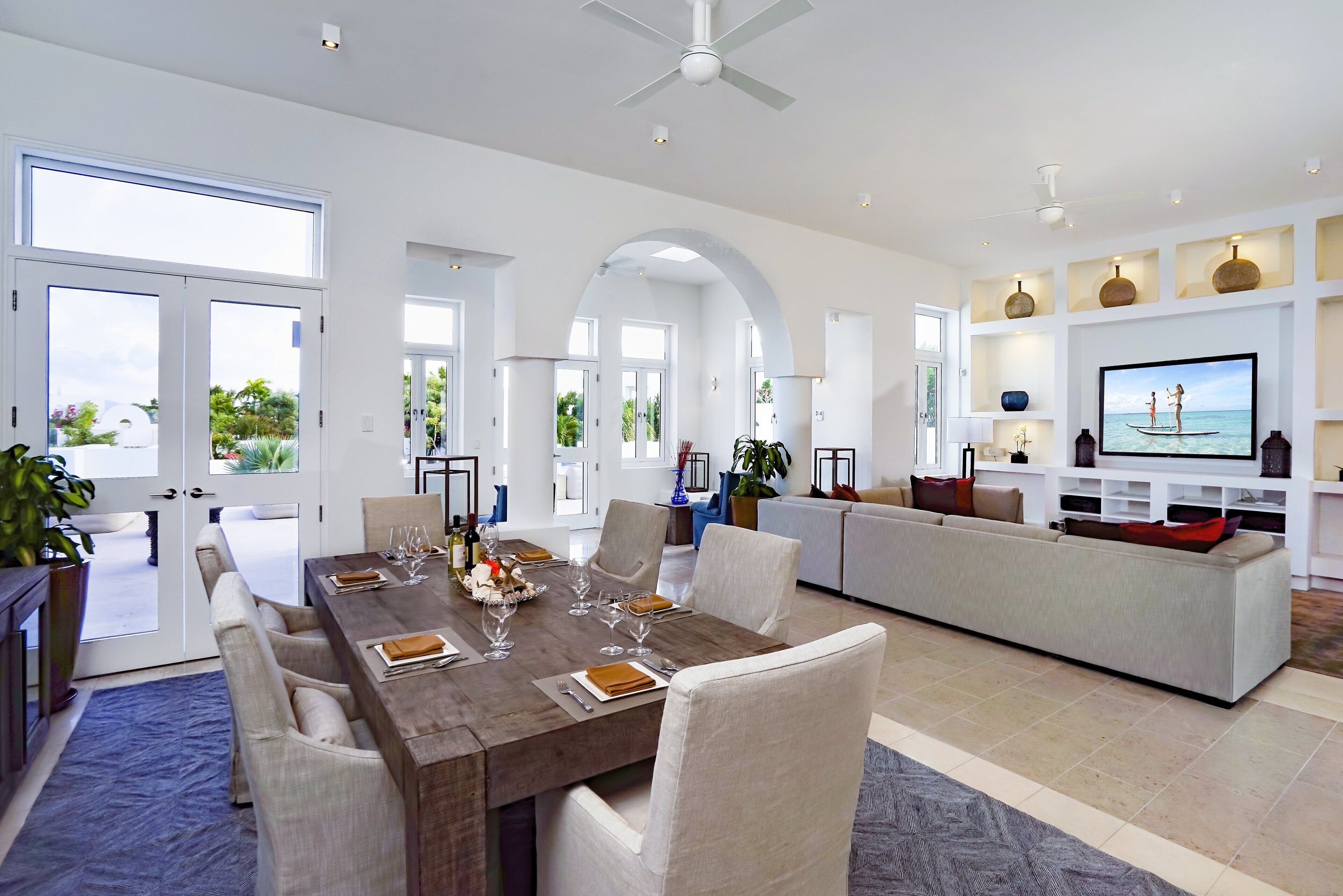 A modern dining area with a wooden table set for six, surrounded by white chairs, and a large flat-screen TV mounted on the wall.