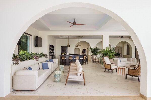 A spacious living area with a white sofa, a coffee table, and a dining table with chairs. There is a kitchen area in the background with a bar and seating. - Aurora Anguilla Resort & Golf Club (Rendezvous Bay)