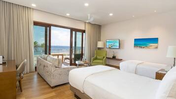 A hotel room with a large window, a sofa, two beds, a desk, a chair, and a TV.