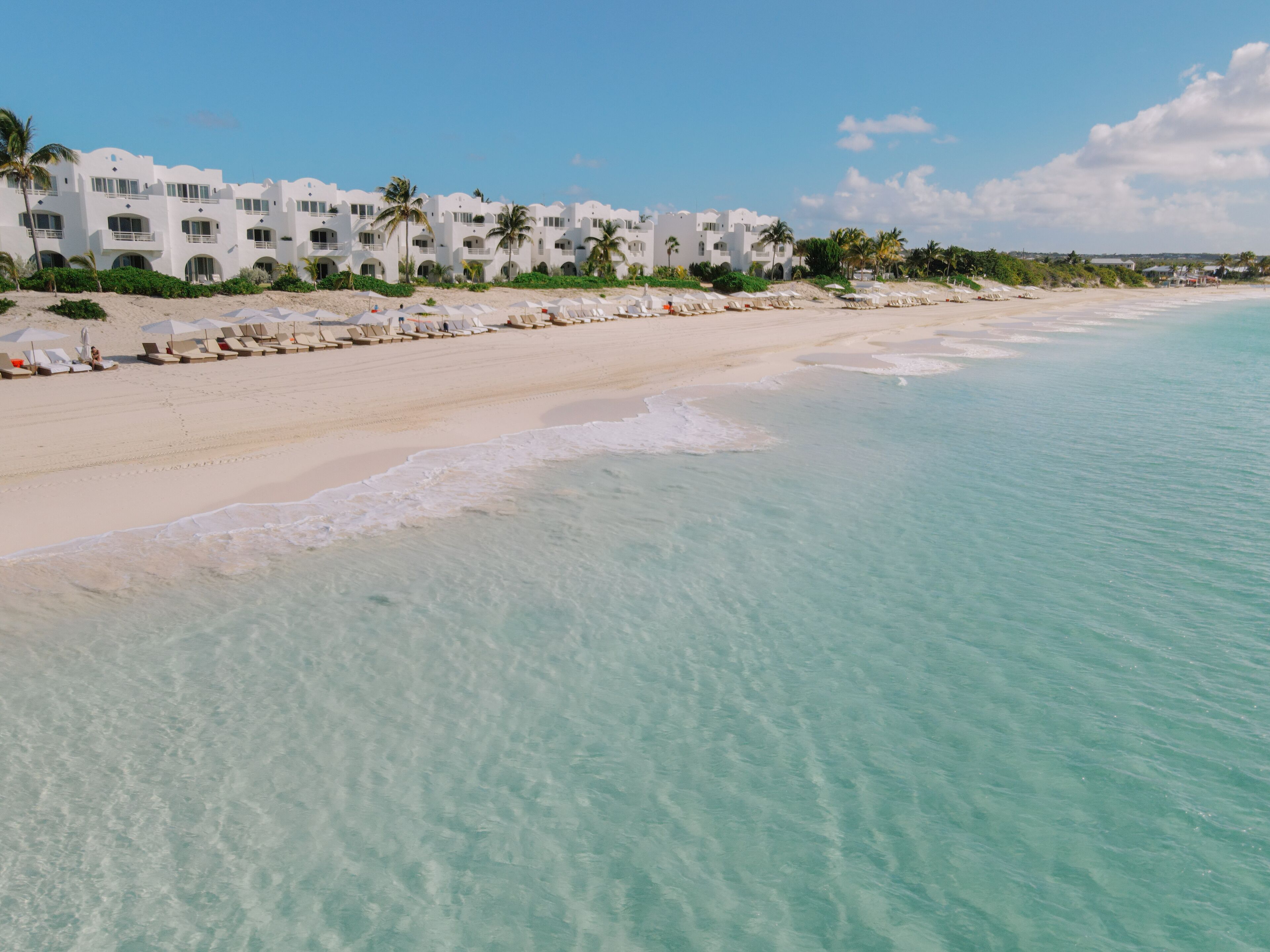 A beachfront hotel with multiple balconies, a sandy beach, and clear turquoise waters.