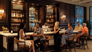 A bar area with a counter, stools, and shelves of bottles and glasses.