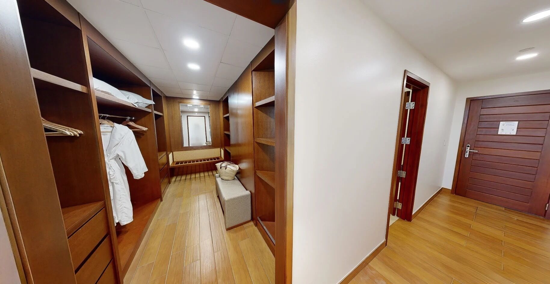 A walk-in closet with wooden shelving, a bench, and a mirror.