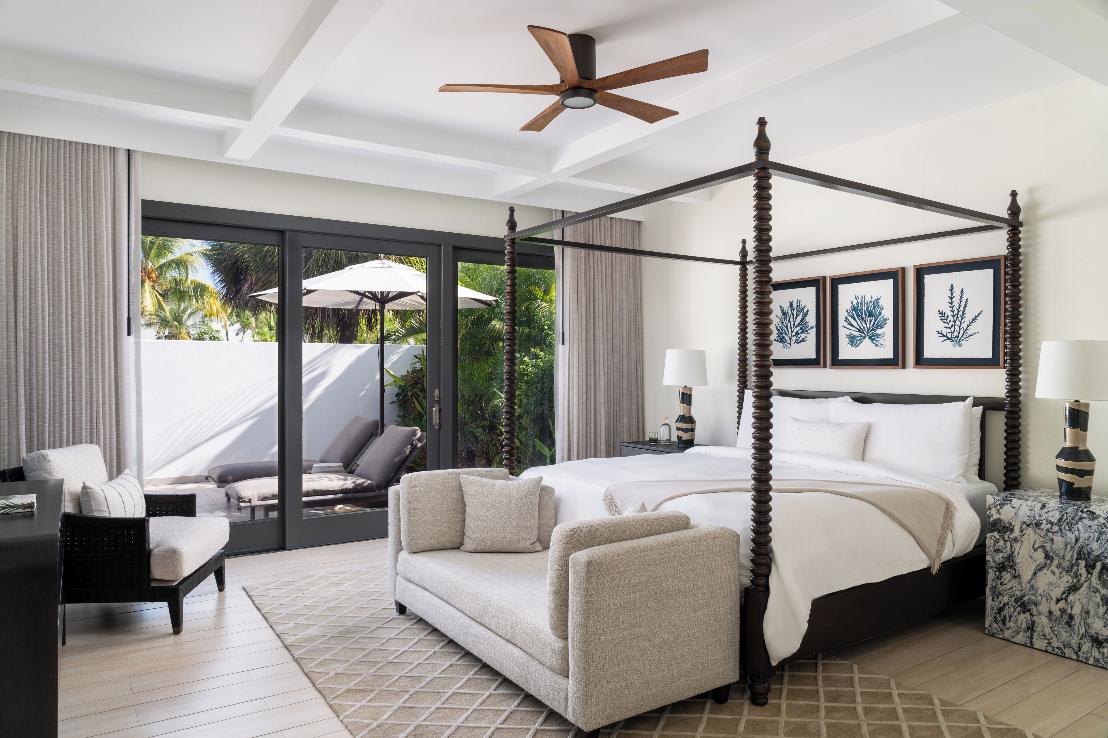 Un dormitorio amplio con cama con dosel, ventilador de techo y ventana grande con vistas a un jardín tropical.