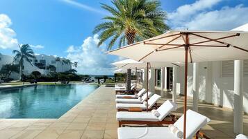 A poolside area with sun loungers, umbrellas, and a palm tree.