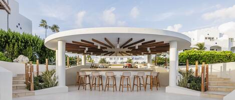 Un área de bar moderna al aire libre con diseño circular, taburetes de madera y vistas del paisaje circundante.