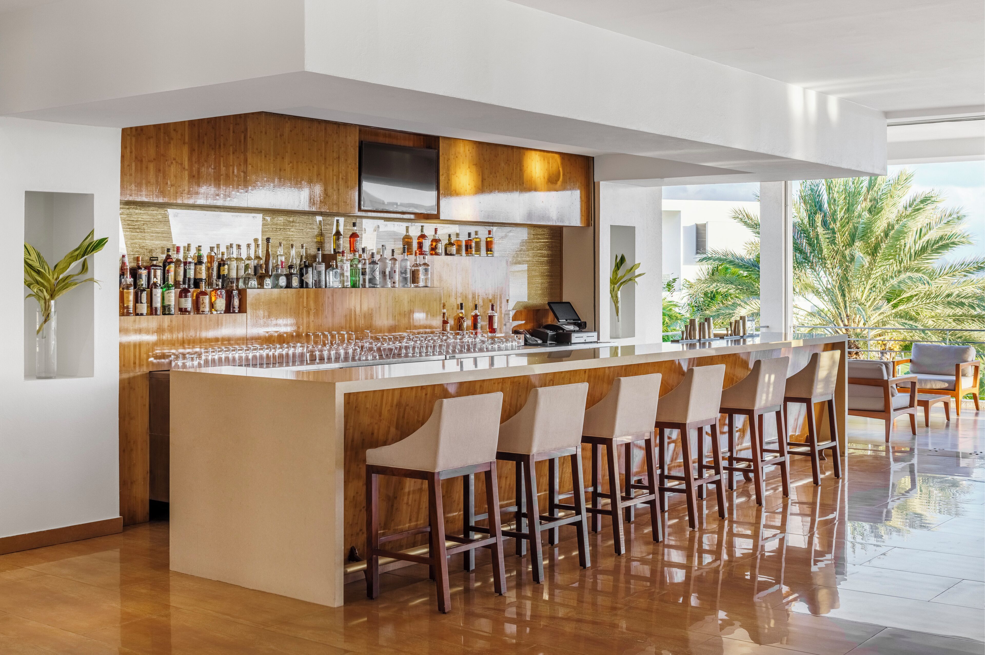 A modern bar area with a wooden bar counter, multiple stools, and a variety of bottles.