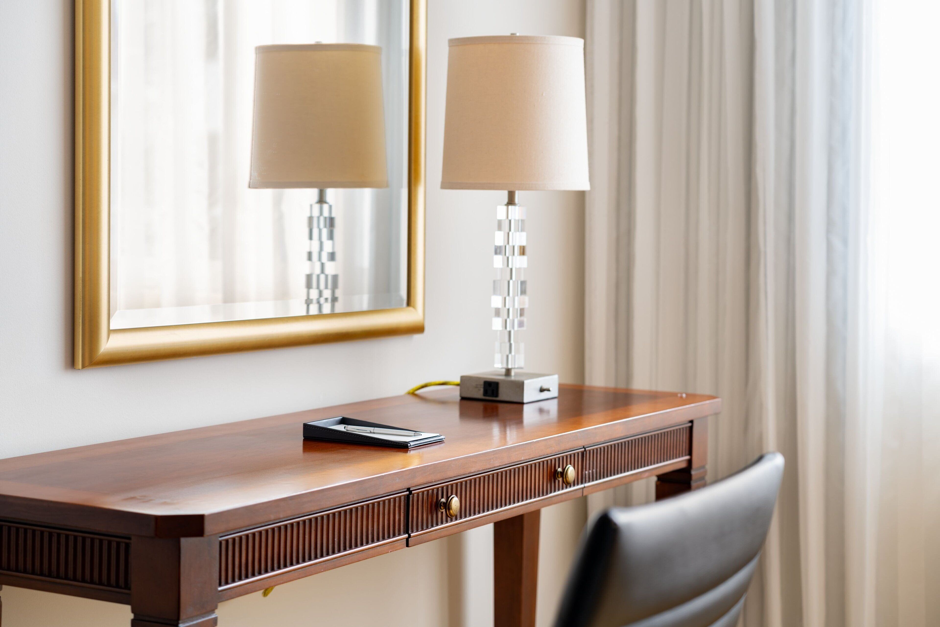A wooden desk with a lamp, a mirror, and a small electronic device.