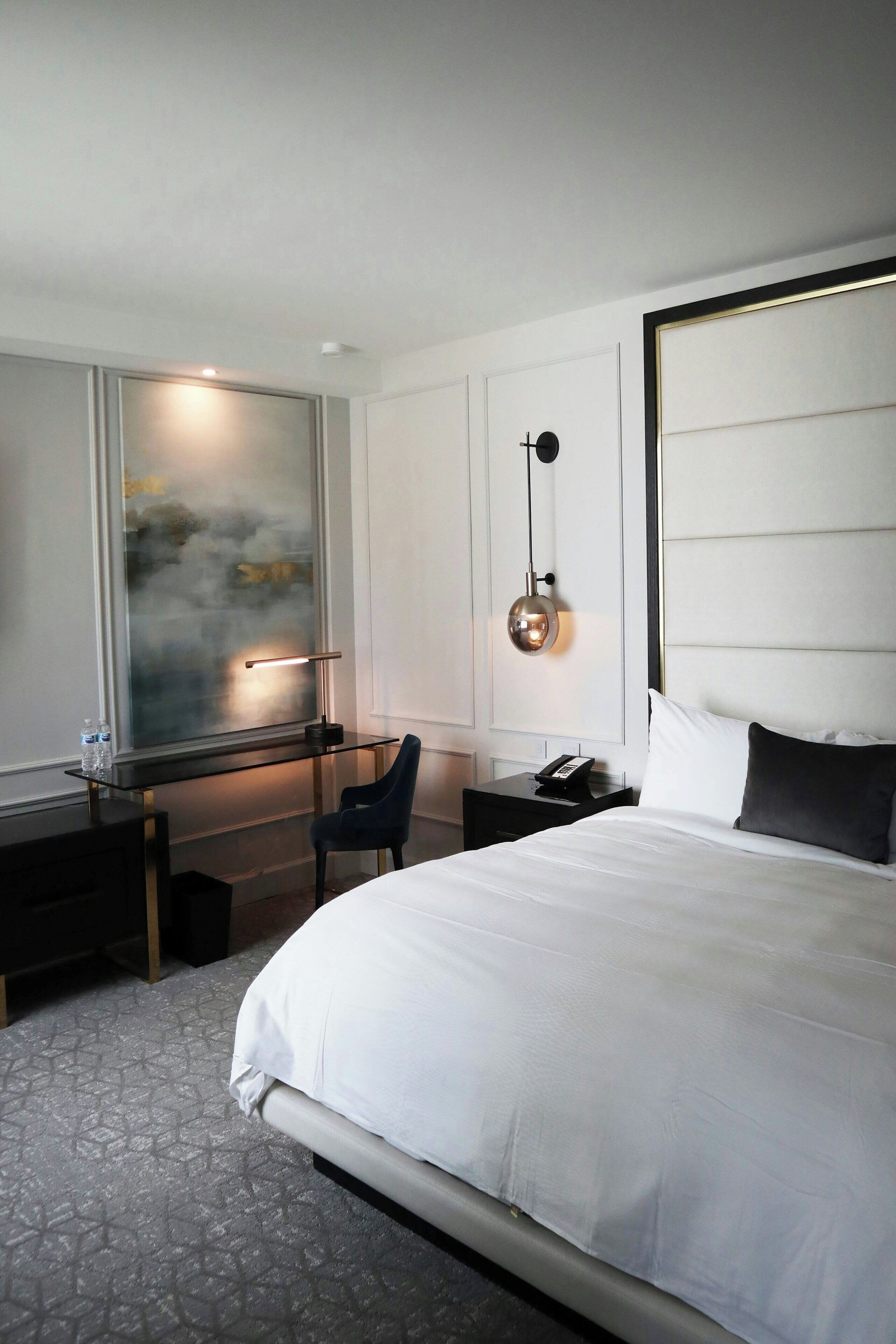 Et moderne hotelværelse med en stor seng, et skrivebord, en stol og et stort vindue med udsigt.