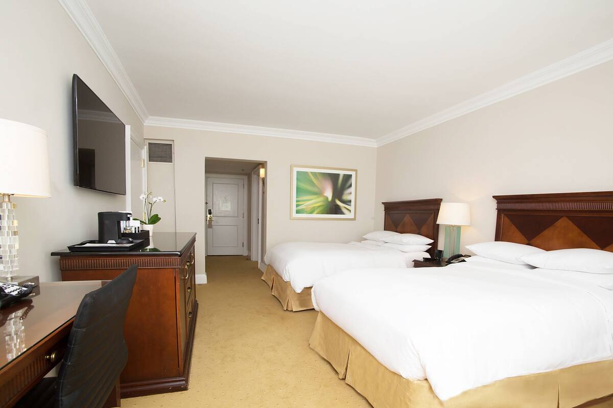 Ein Hotelzimmer mit zwei Betten, einem Schreibtisch mit Stuhl, einem Fernseher und einem Bild an der Wand.