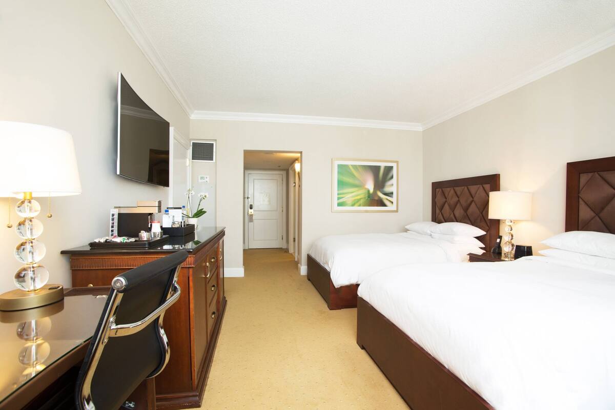 Ein Hotelzimmer mit Bett, Nachttisch, Lampe, Schreibtisch, Stuhl, Fernseher und einem Bild an der Wand.