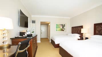 Une chambre d’hôtel équipée d’un lit, d’une table de chevet, d’une lampe, d’un bureau, d’une chaise, d’une télévision et d’une œuvre d’art au mur.