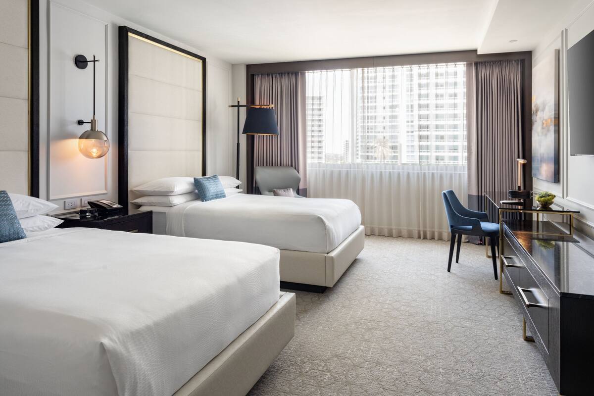 Ein Hotelzimmer mit zwei Betten, einem Schreibtisch und einem großen Fenster mit Vorhängen.