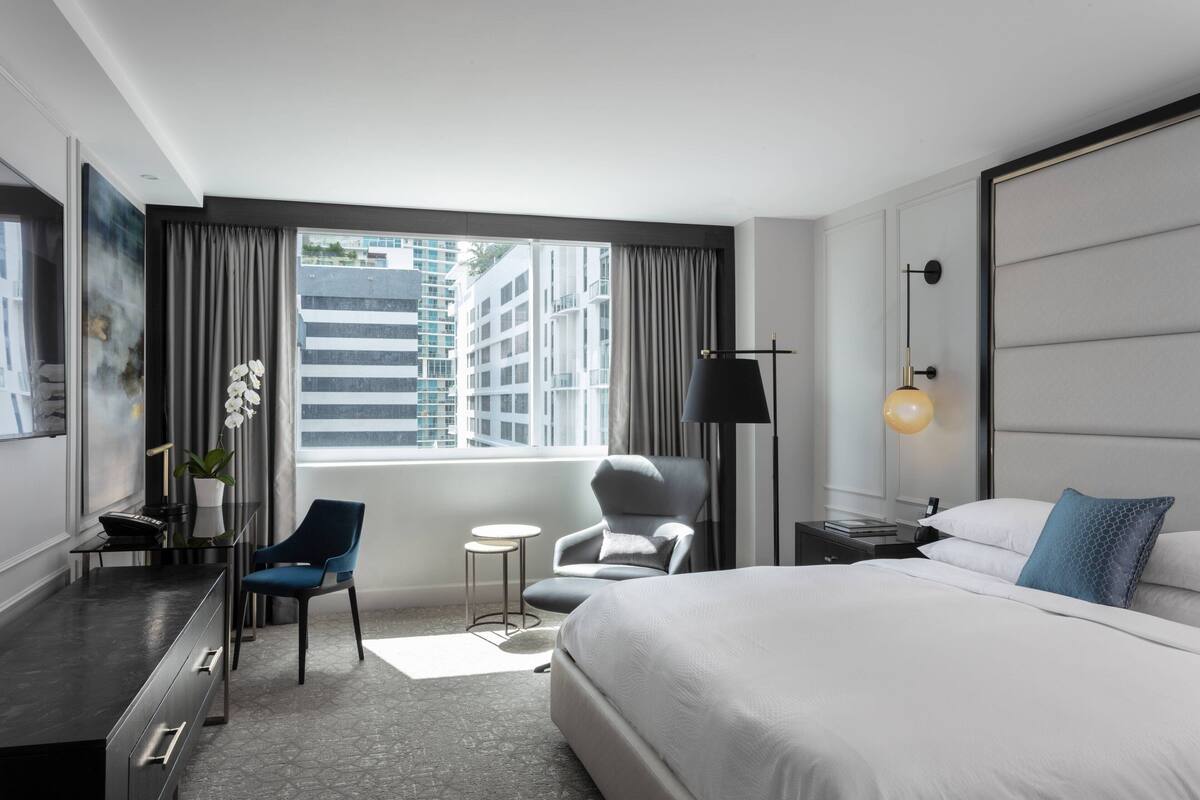Ein modernes Hotelzimmer mit einem großen Bett, einem Schreibtisch mit Stuhl, einem kleinen Tisch und einer Lampe.
