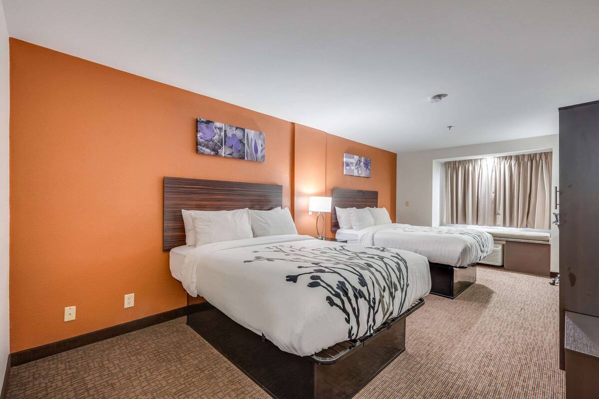 A hotel room with two beds, a large window with curtains, and artwork on the walls.