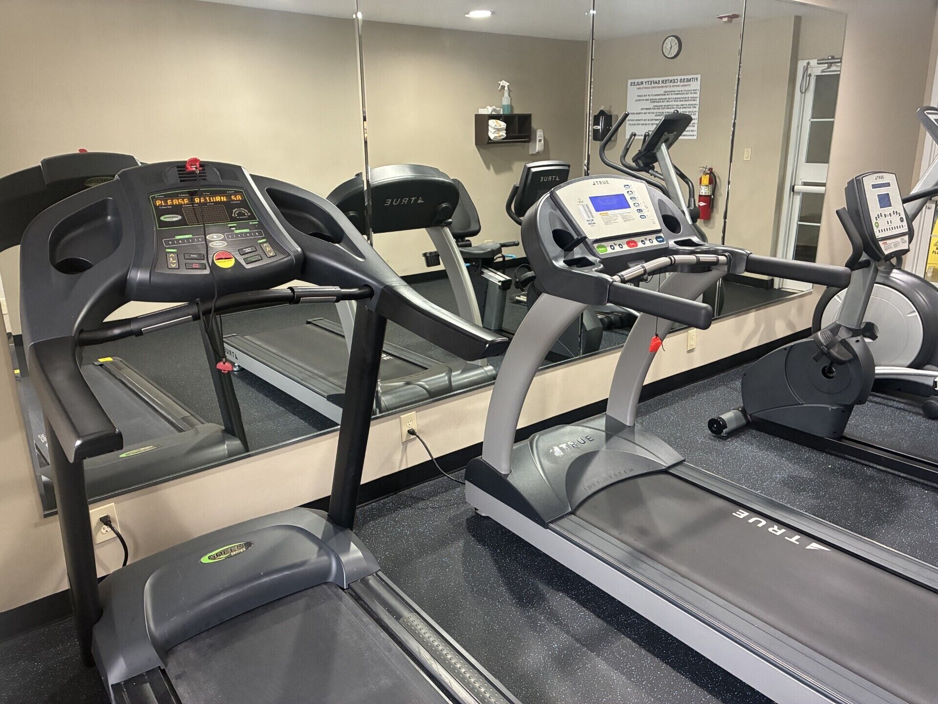 A gym with multiple treadmills, a mirrored wall, and a clock.