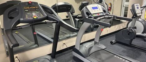 A gym with multiple treadmills, a mirrored wall, and a clock.