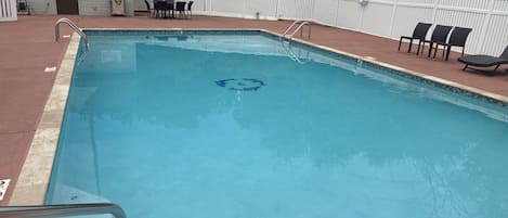 A rectangular swimming pool with a white fence, a pool ladder, and a few lounge chairs.