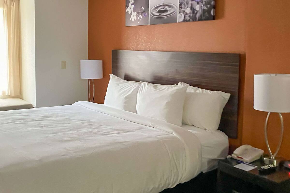 A hotel room with a large bed, a nightstand with a lamp, and a wall-mounted phone.