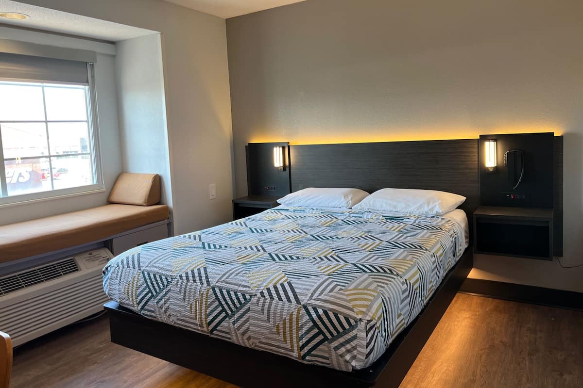 A modern hotel room with a large bed, a bench by the window, and a wall-mounted TV.