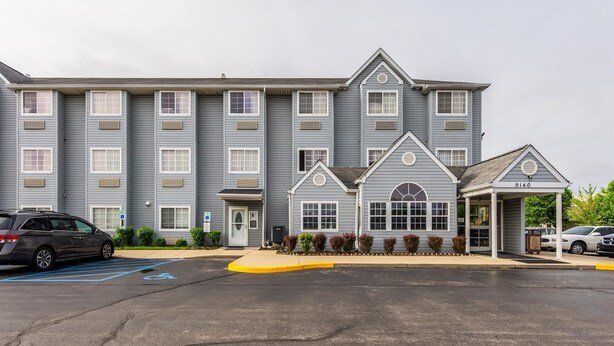 A multi-story hotel with a central entrance, a parking lot, and a few cars parked. - Motel 6 Indianapolis Carmel (Indianapolis)