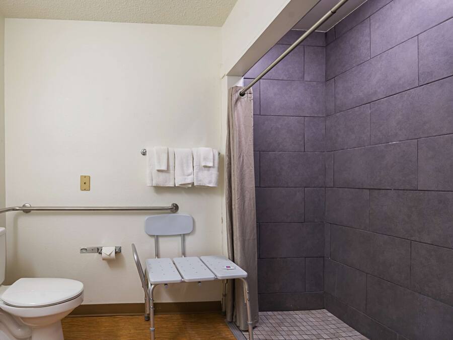 A bathroom with a toilet, a shower with a curtain, a grab bar, and a small table.