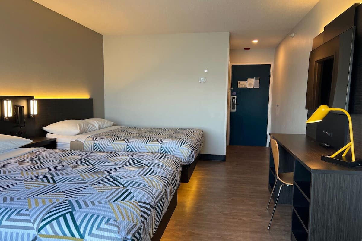 A hotel room with two beds, a desk, a chair, and a TV.