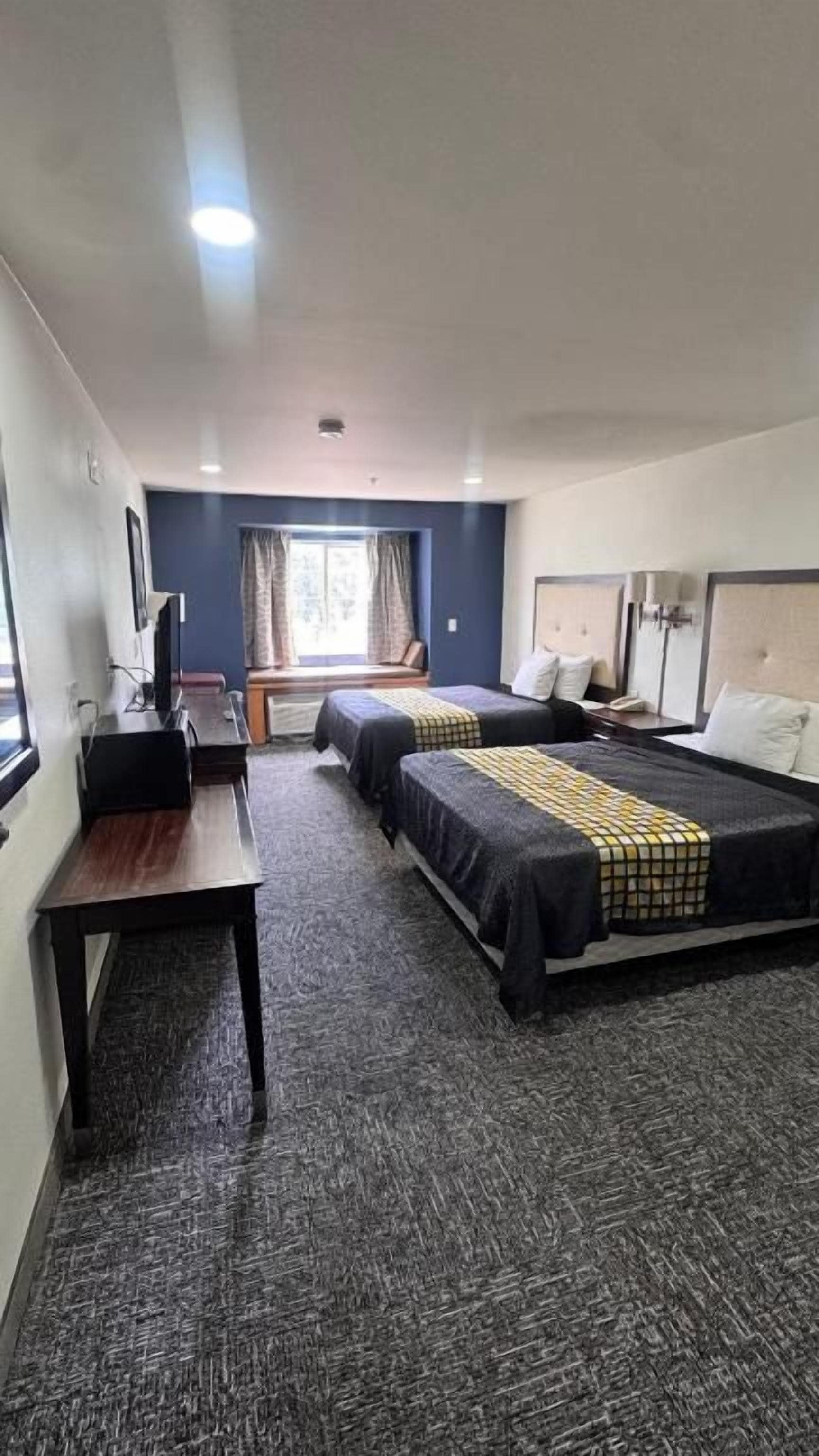 A hotel room with two beds, a desk, and a window with curtains.