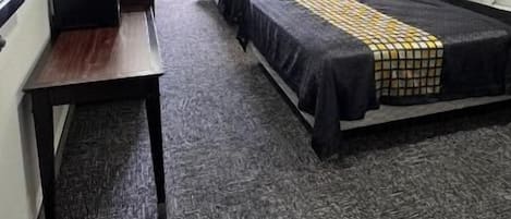 Ein Hotelzimmer mit zwei Betten, einem Schreibtisch und einem fensterbepflanzten Fenster.