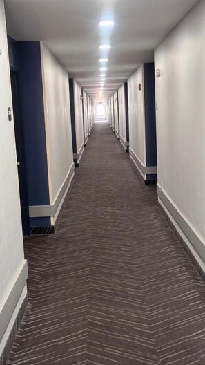 Un pasillo largo y estrecho en un hotel, con puertas a ambos lados y piso alfombrado.