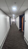 Un largo y estrecho pasillo de hotel con alfombra estampada, paredes blancas y puertas a ambos lados.