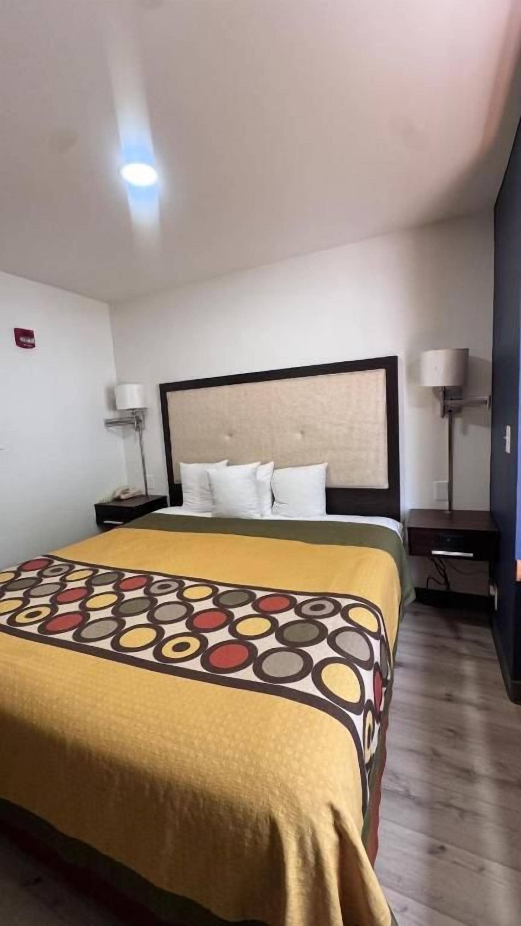A hotel room with a bed, bedside tables, lamps, and a patterned bedspread.