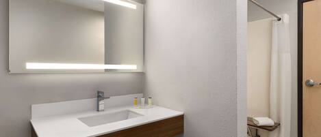 A modern bathroom with a white sink, wooden vanity, and a large mirror with integrated lighting.