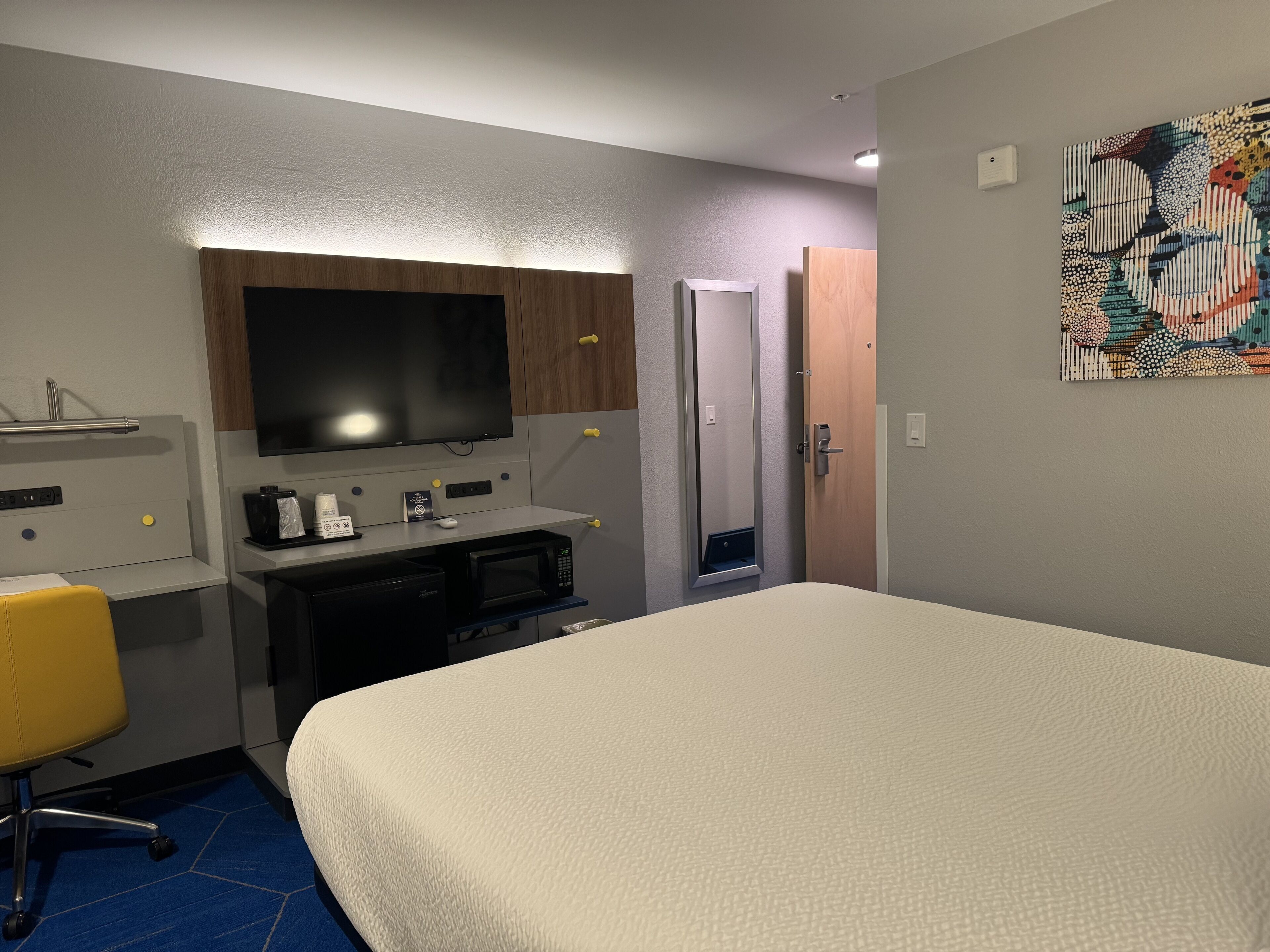 A hotel room with a bed, a desk with a computer, a television, and a microwave.