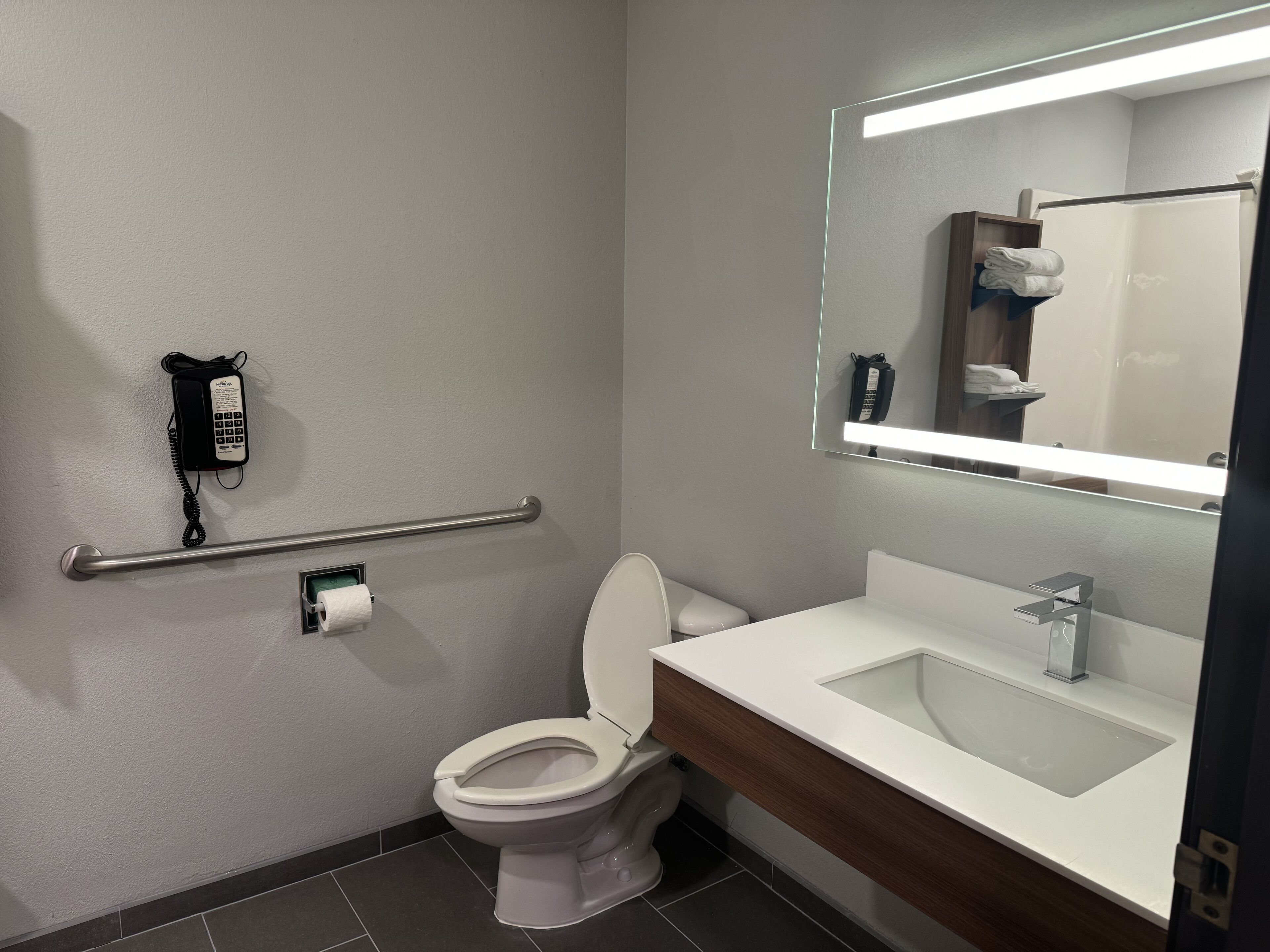 A modern bathroom with a toilet, a handrail, a sink, and a mirror.