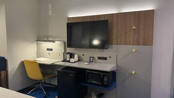 A hotel room with a desk, chair, television, minibar, and a small coffee maker.