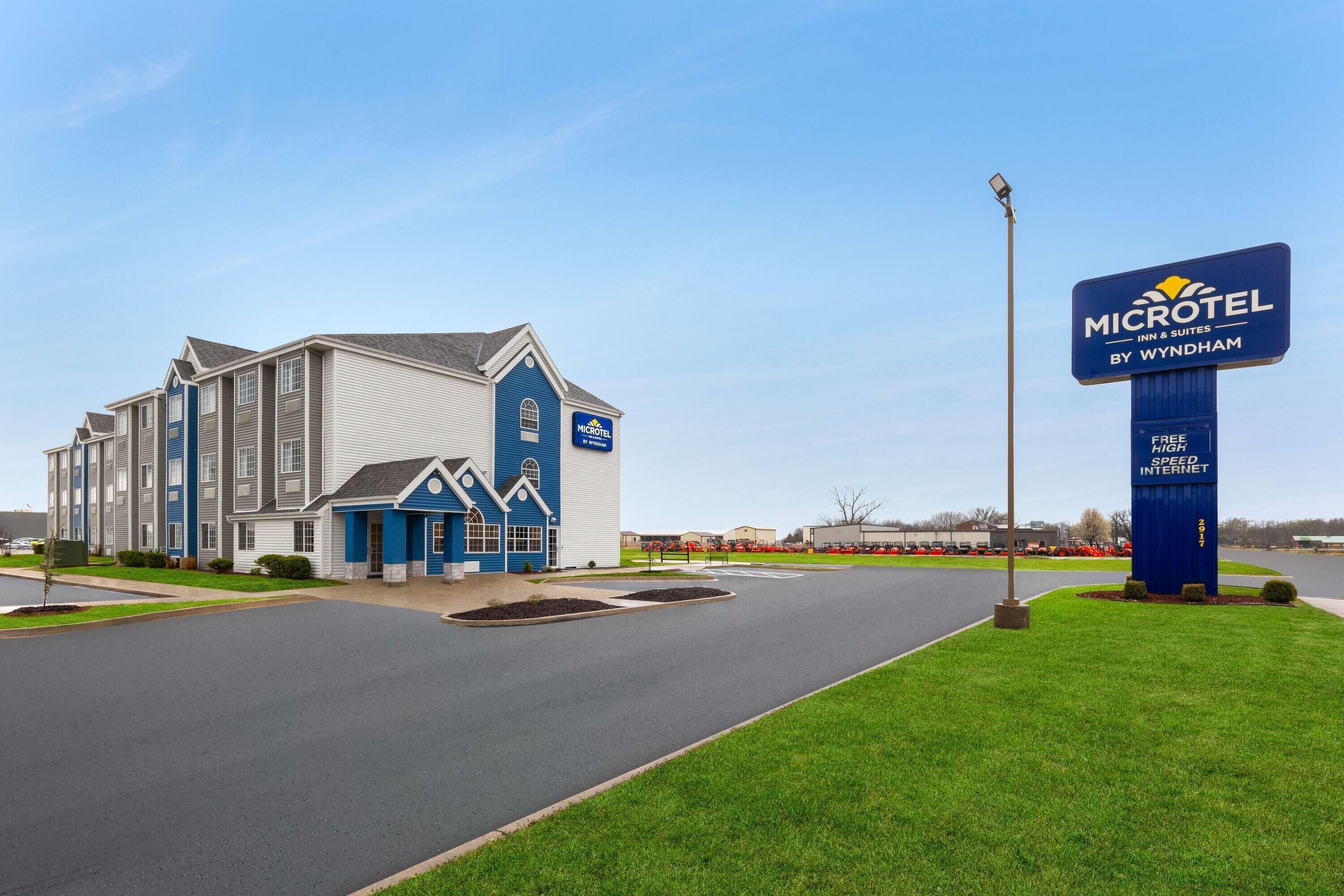 A Microtel Inn & Suites building with a blue and white exterior, a large signboard, and a well-maintained lawn area.