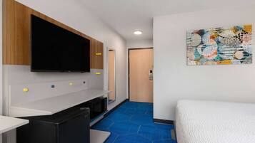 A hotel room with a bed, a desk with a flat-screen TV, a microwave, and a door leading to another room.