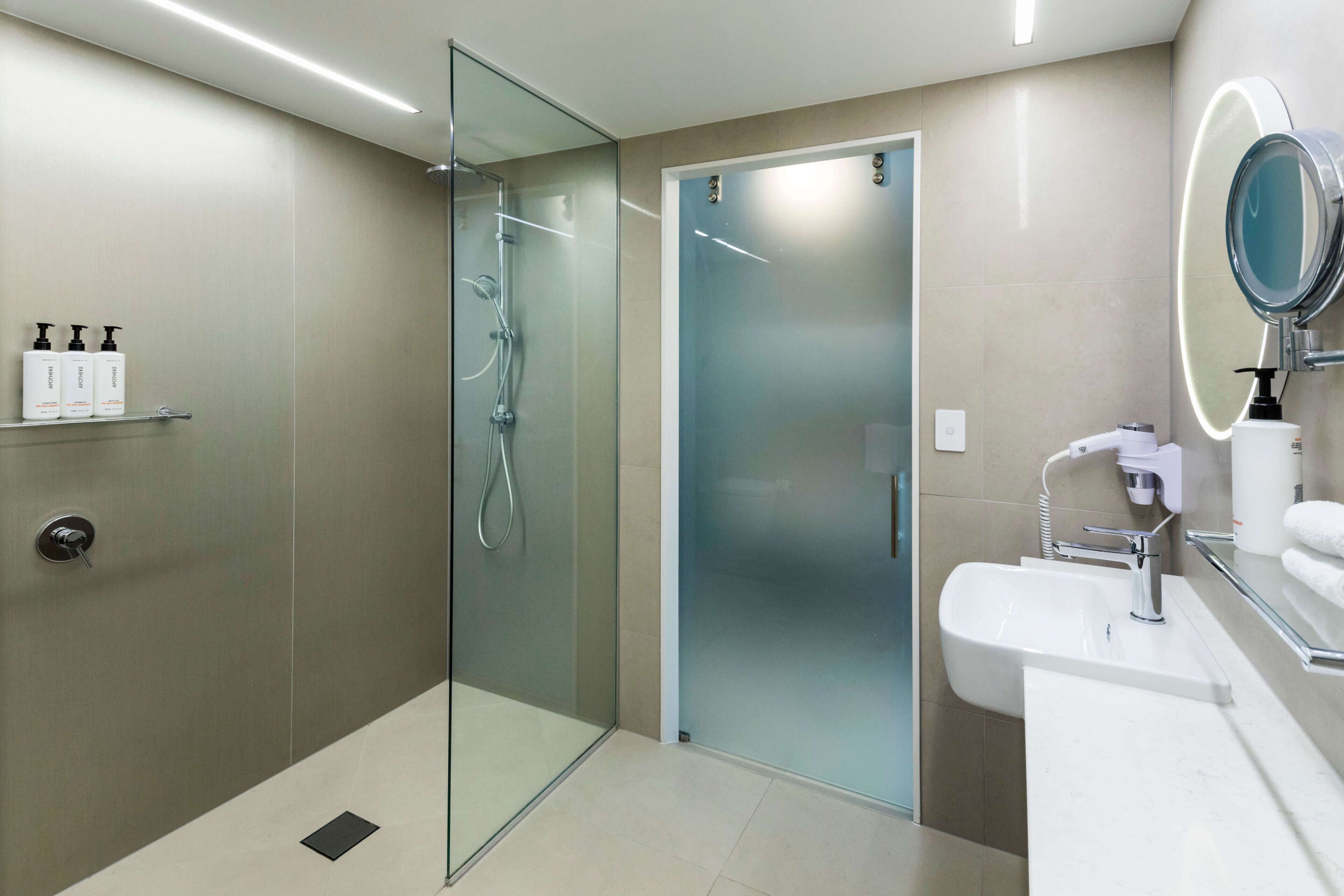 A modern bathroom with a glass-enclosed shower, a sink with a mirror, and toiletries on a shelf.