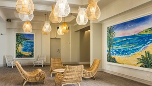 Una habitación con mobiliario de mimbre, grandes cuadros de una playa y múltiples lámparas colgantes.